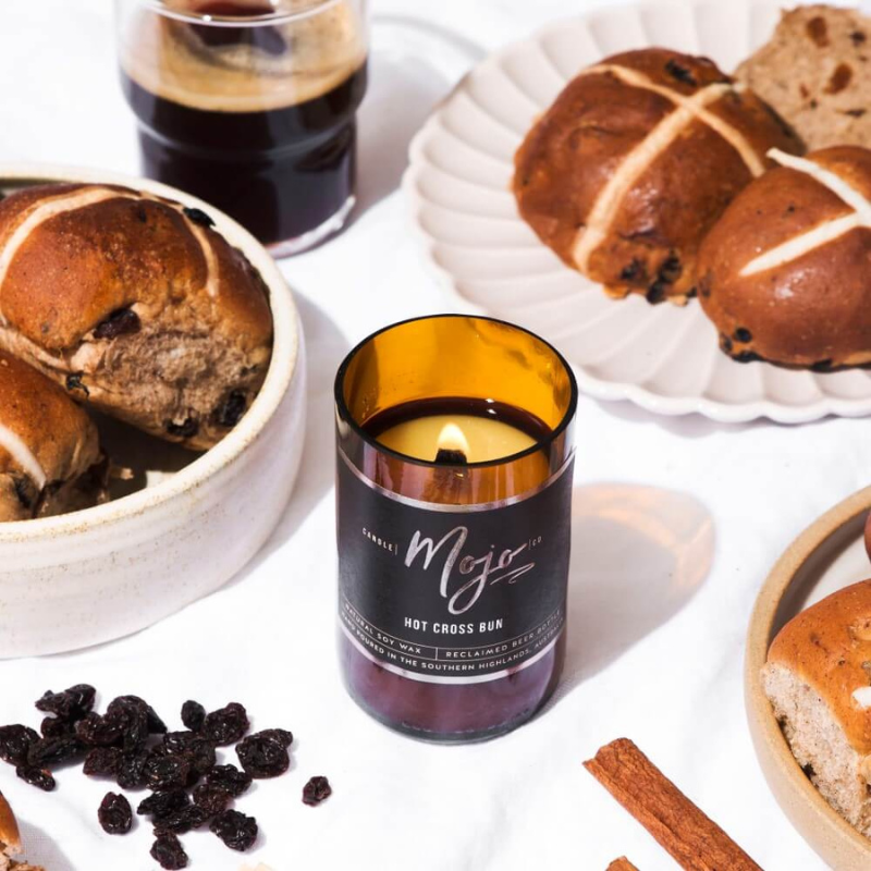 Mojo Candle Co's Hot Cross Bun Candle surrounded by sultanas, hot cross buns and cinnamon.