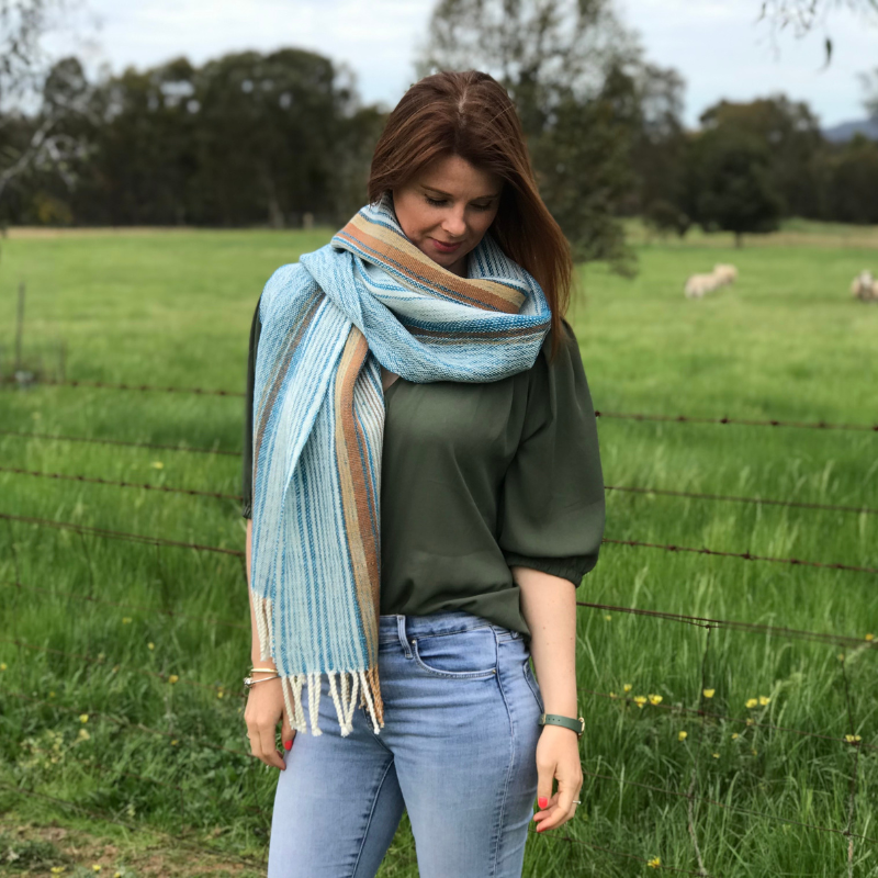 A woman standing in a field wearing a blue and brown Ashculme Textiles scarf 