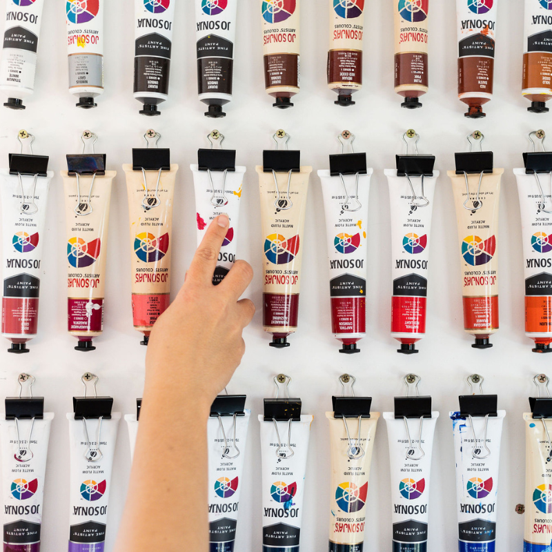 The hand of Sarah Richards grabbing one of her paints from a range of different colour options