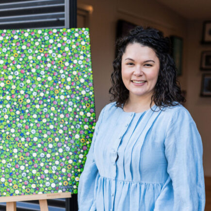 Photo of Sarah Richards, a contemporary Aboriginal artist standing in front of one of her artworks